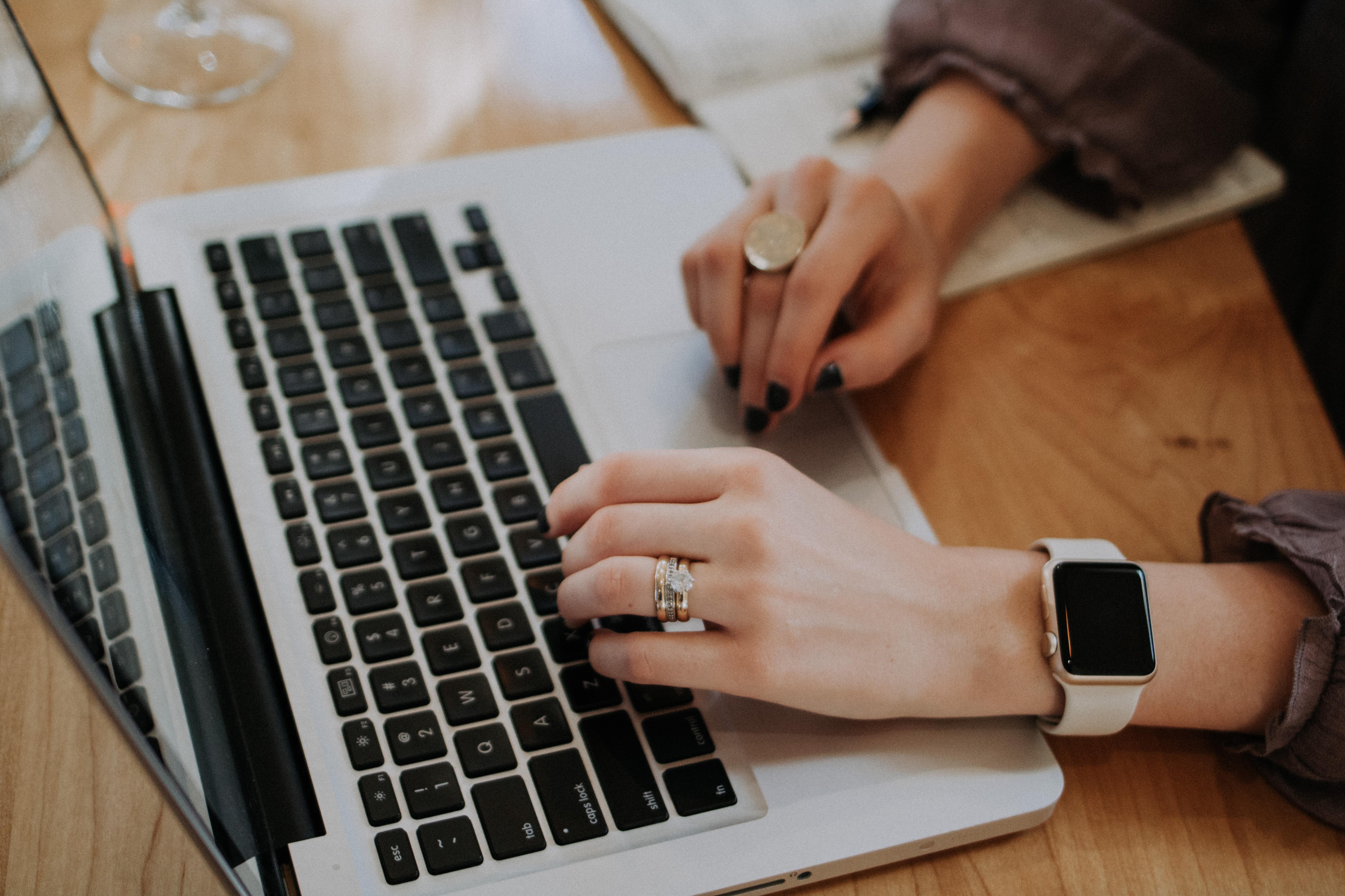 Mão femininas em um ambiente de escritório está a mexer em um notebook aberto.