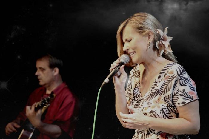 Uma moça cantando no palco ao lado de um guitarrista