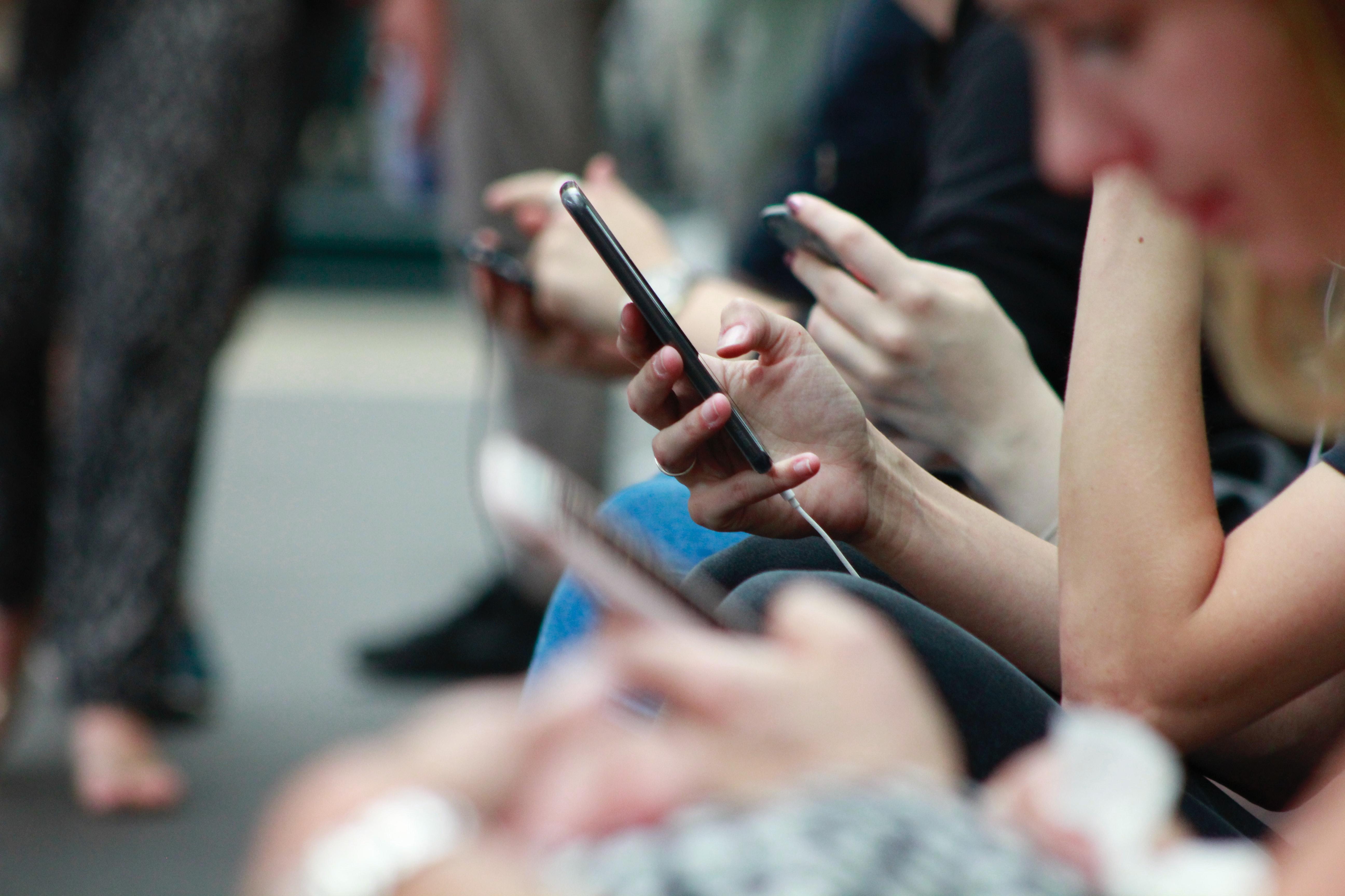 Em linha, vemos jovens mulheres segurando smartphones, concentradas nos dispositivos.