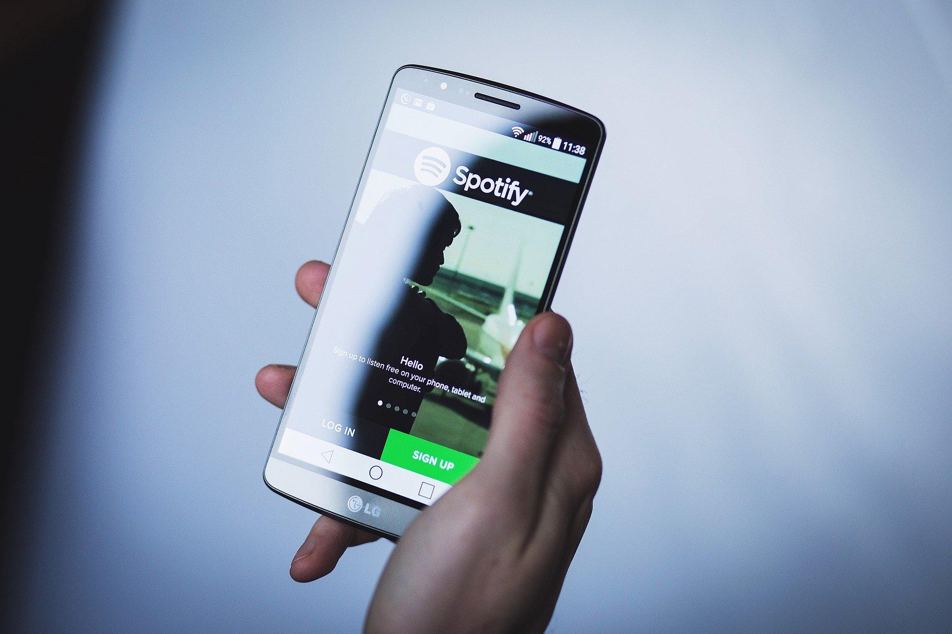 Mão segura um smartphone com o aplicativo do Spotify aberto em destaque na tela.
