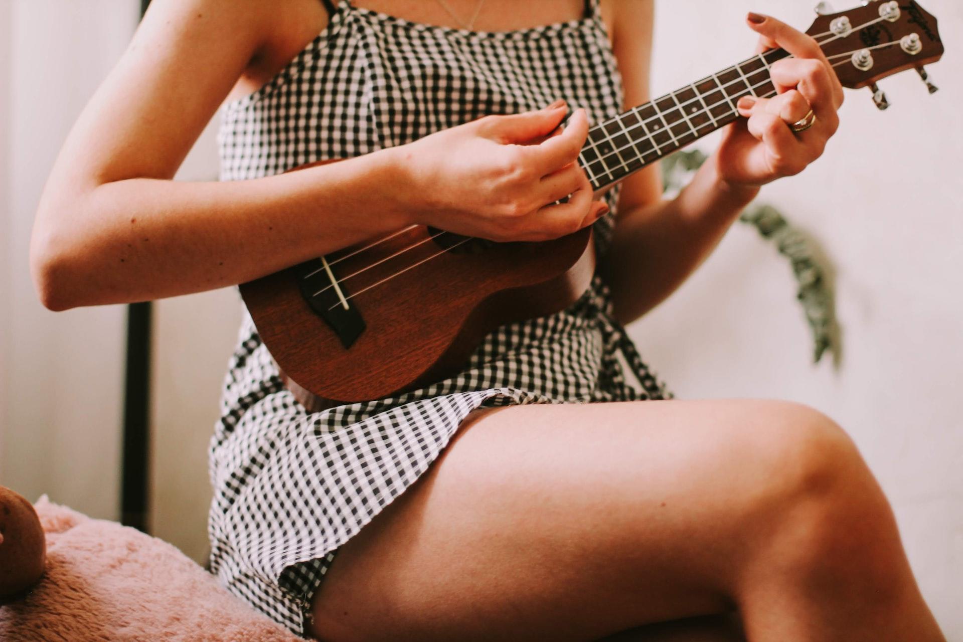 mulher sentada no braço de um sofa tocando ukulele