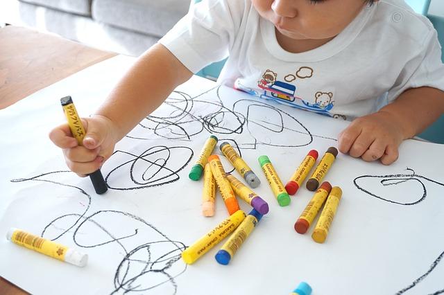 Criança faz desenho sobre papel com lápis de cêra.