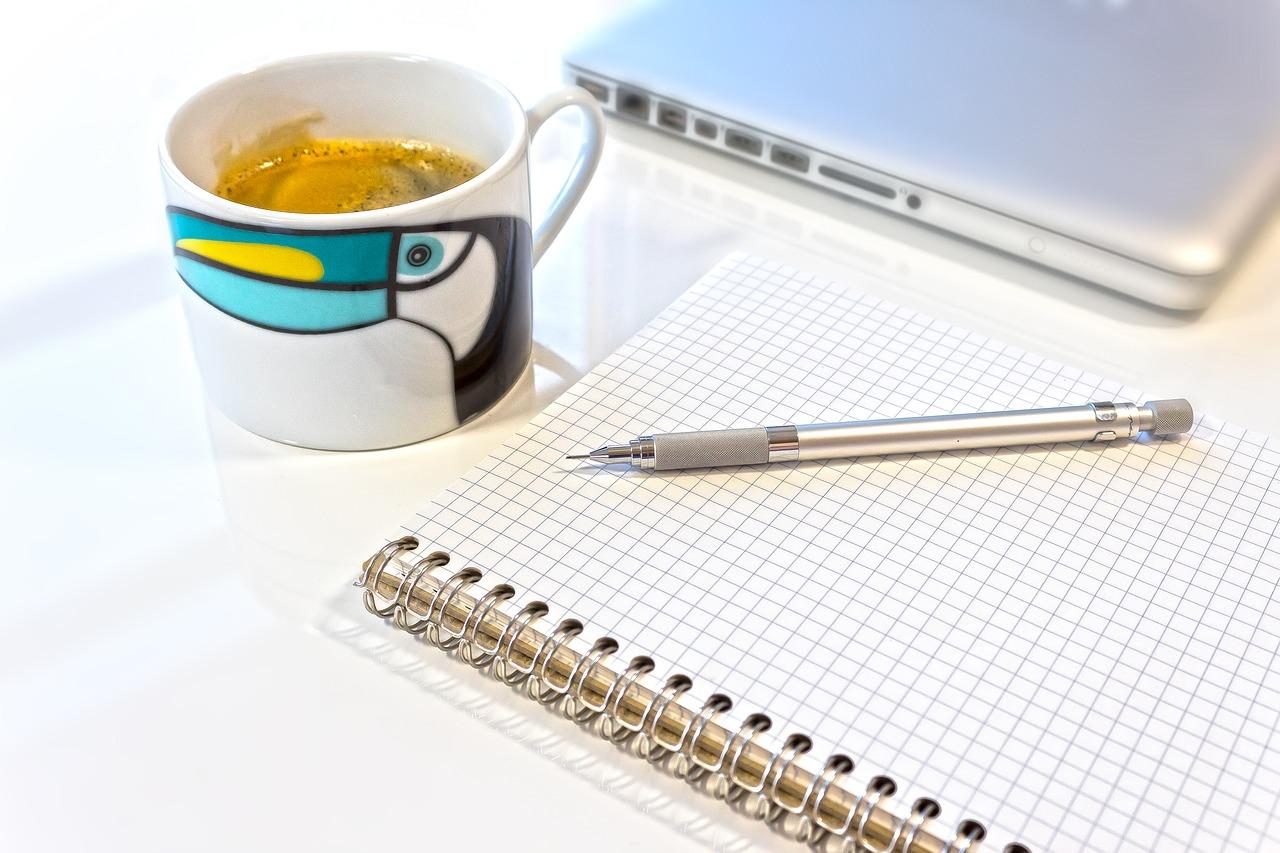 Um computador, um café e um bloco de desenho