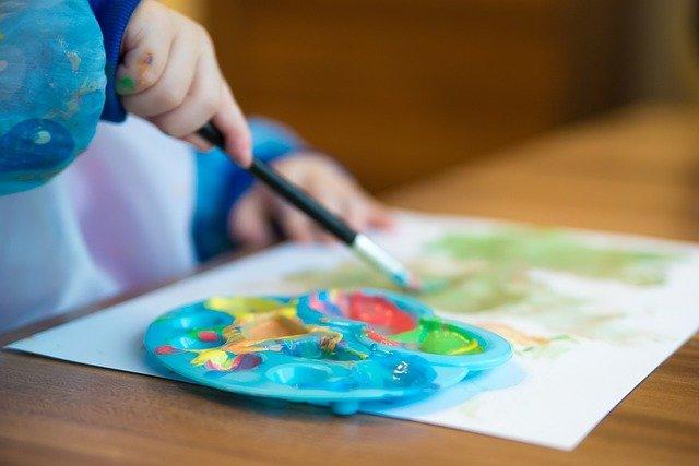 Criança pintando com pincel e godê de tinta.