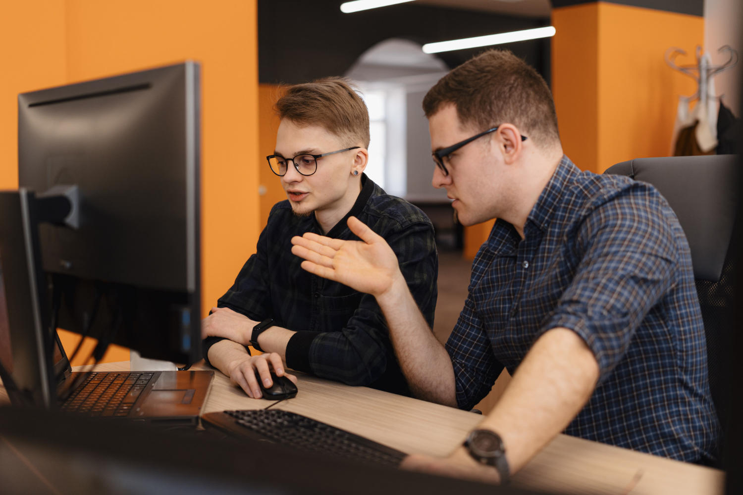 Homem conversando com outro e apontando para o computador.
