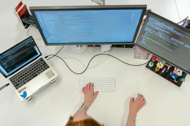 Pessoa trabalhando com programação na frente de 3 telas de computador