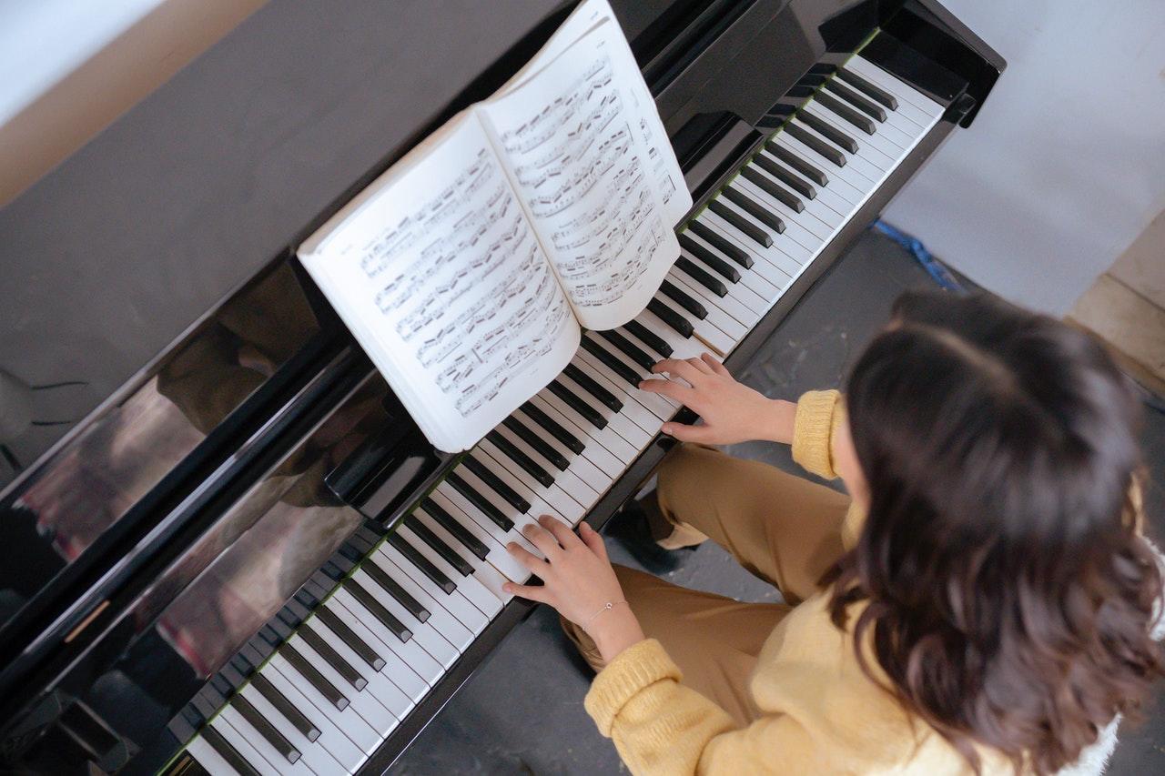 Moça tocando piano acompanhando uma partitura.