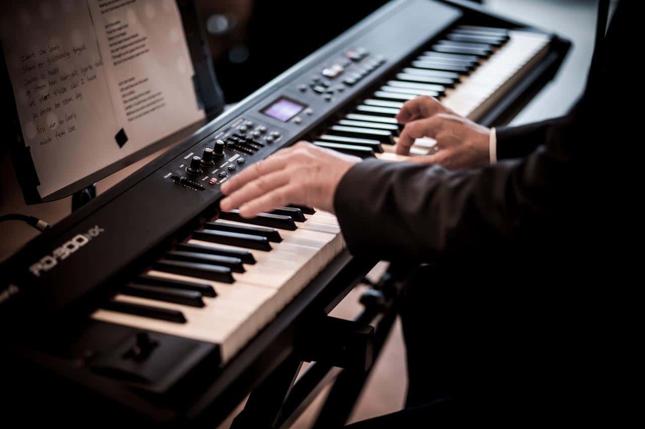 Imagem de um teclado eletrônico com uma pessoa executando uma música.