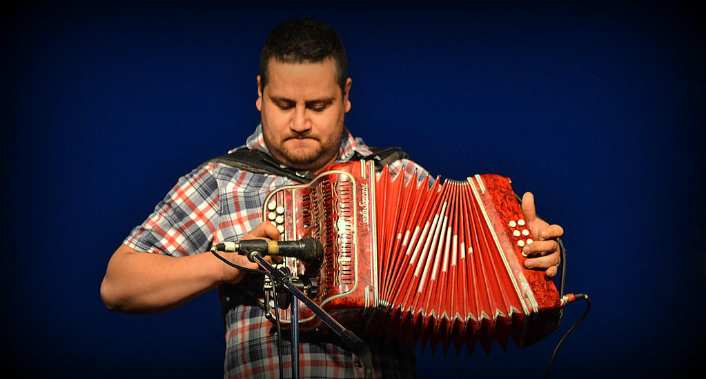 Homem tocando um acordeon vermelho.