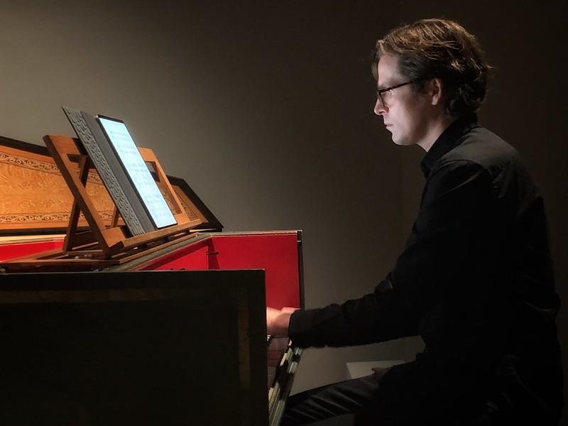 Rapaz, vestido de preto, tocando o instrumento cravo é uma apresentação de recital.