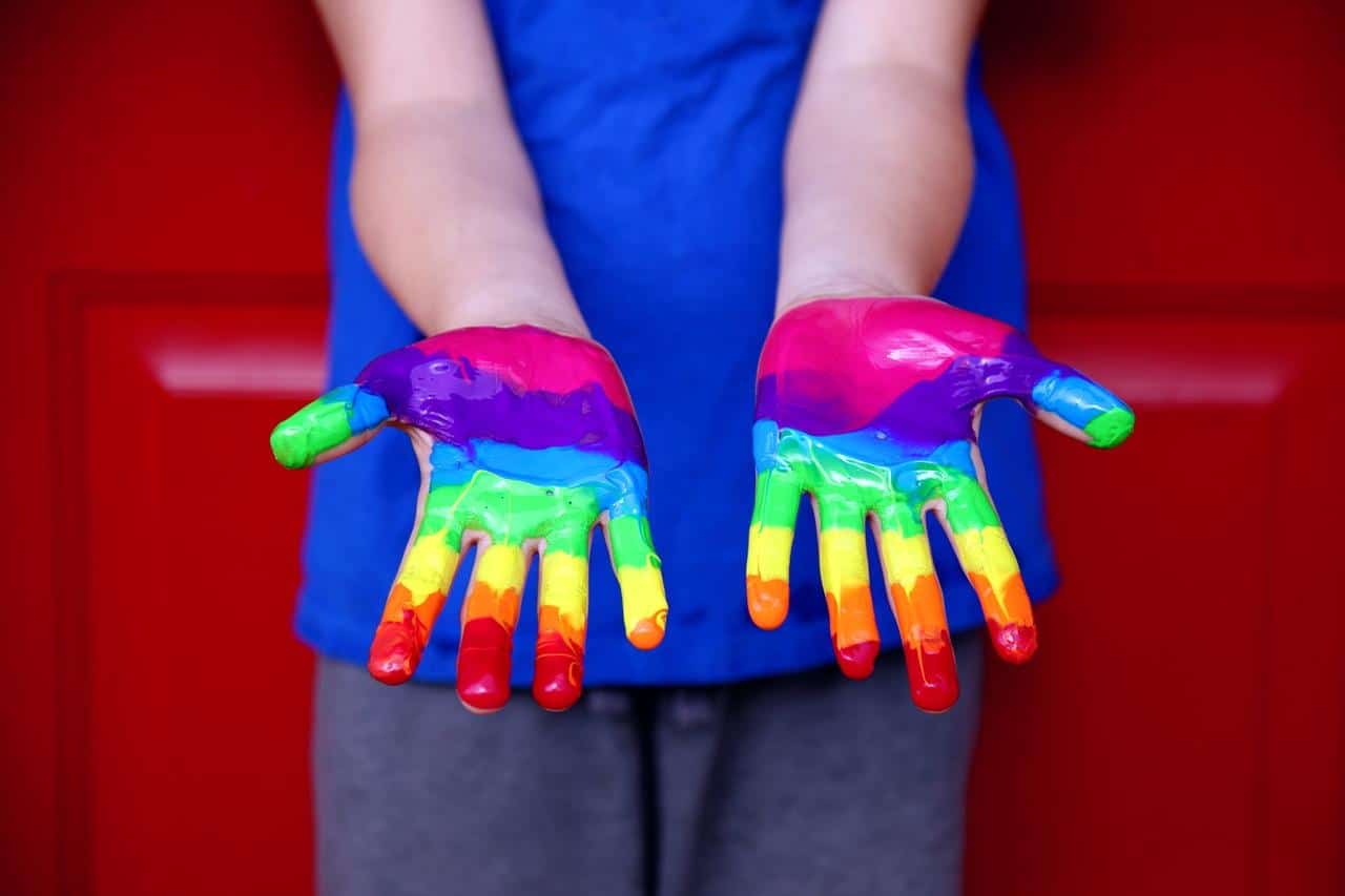 Uma criança com as mãos colorizadas de arco-íris lgtb+