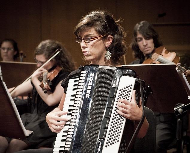 Mulher tocando acordeon em meio a uma orquestra.