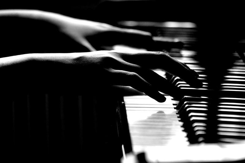 Imagem em branco e preto de mãos de uma pessoa tocando piano.