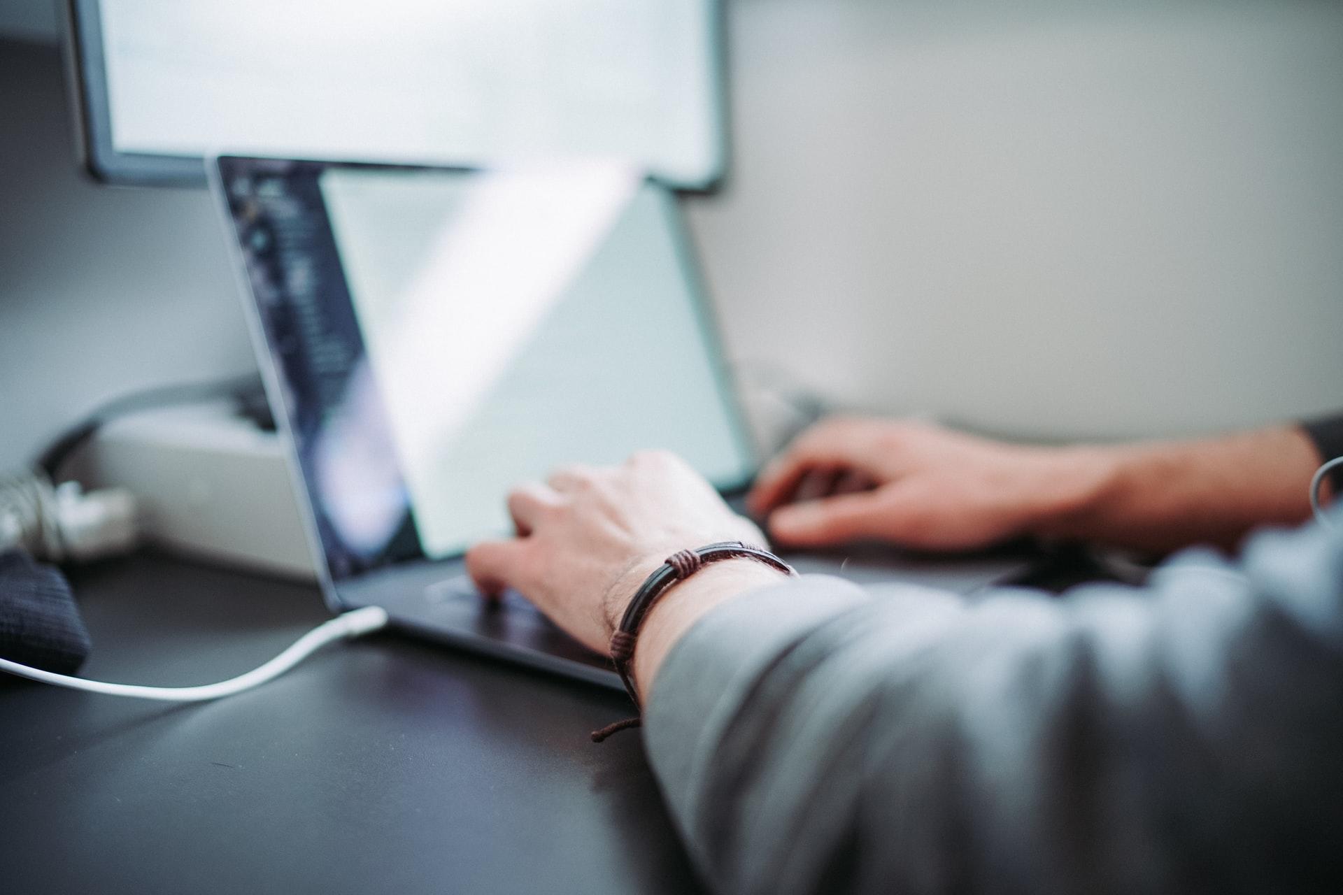 Imagem meio desfocada mostra um notebook e mãos de um programador sobre o dispositivo, denotando que está a programar.