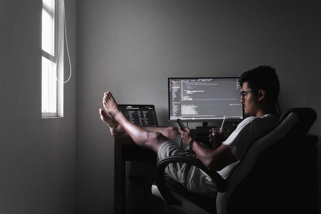 Homem olha no celular enquanto faz programacao no computador