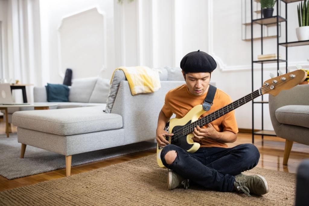 Guitarrista praticando baixo no quarto em casa.