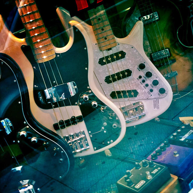 Contrabaixos de vários estilos e modelos expostos em uma vitrine, juntos com pedaleiras de efeitos.