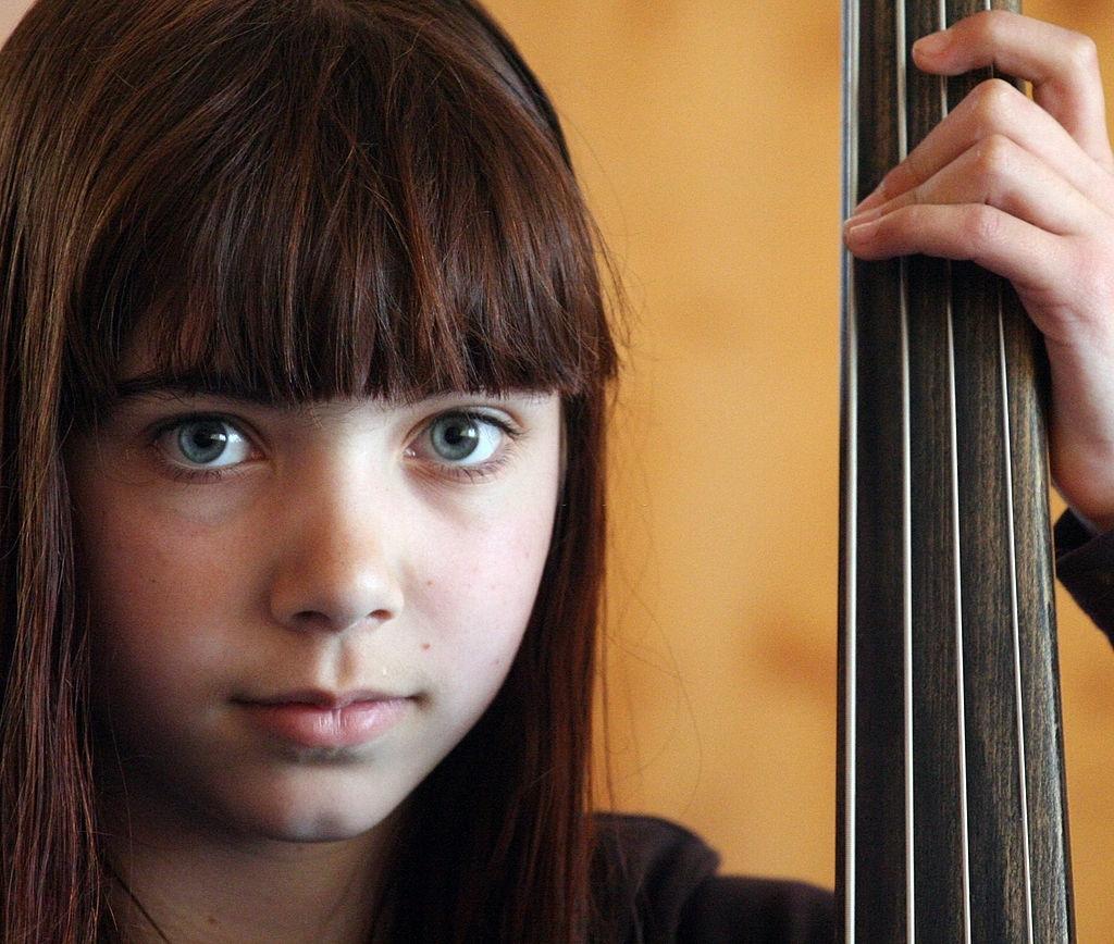 Uma menina de olhos azuis, com a mão nas cordas de um contrabaixo.