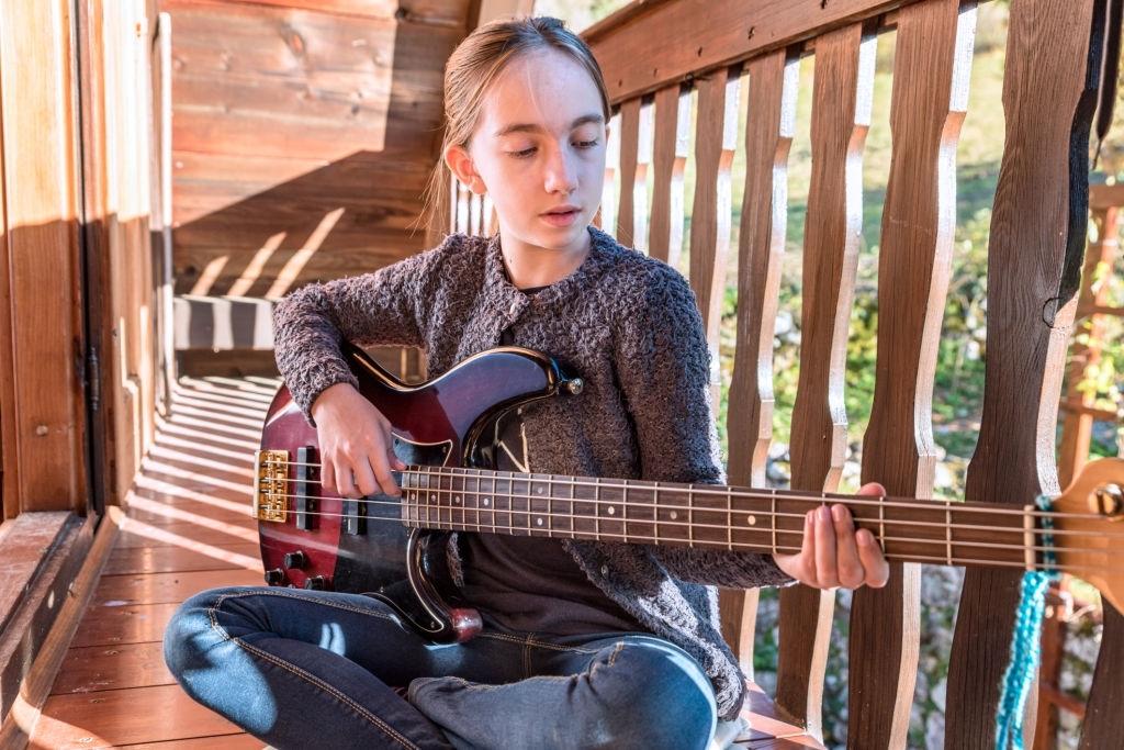 Garota sentada na varanda praticando contrabaixo.