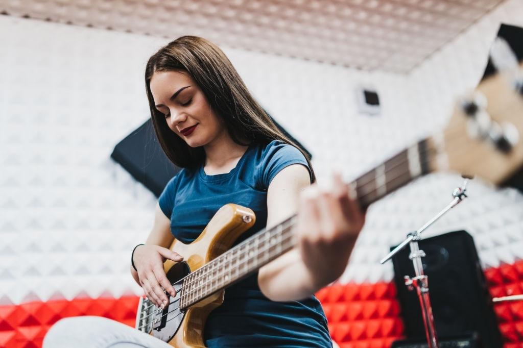 Jovem mulher tocando baixo em estúdio.