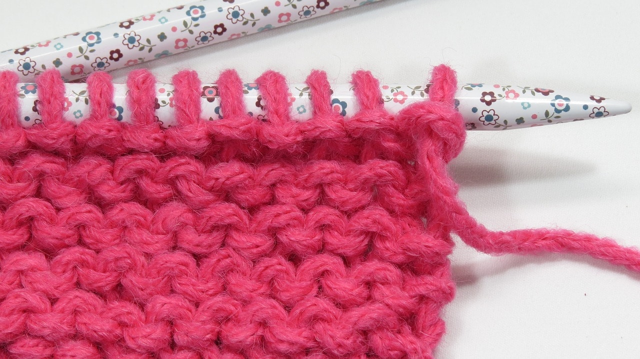 Uma malha de tricô em lã rosa e uma agulha