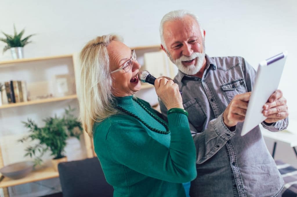 Casal de idosos cantando karaokê em casa, se divertindo.
