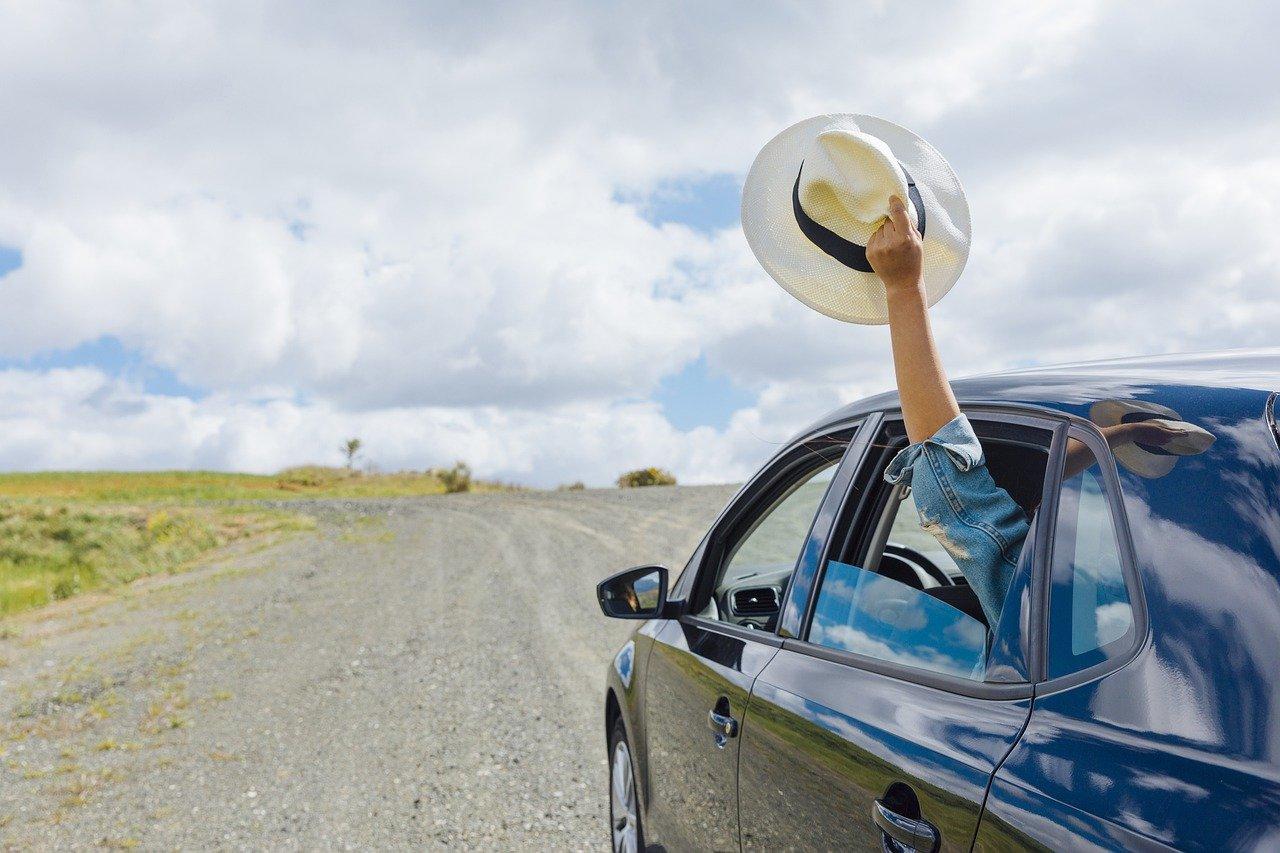 Homem acenando chapéu de dentro de um carro na estrada