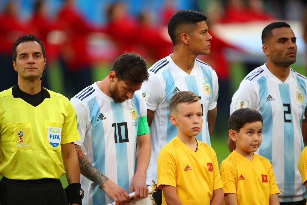Jogadores da Argentina, entre eles, o craque Messi (de cabe baixa) estão perfilados para cantarem o hino nacional antes de mais uma partida. Ao lado está o juiz e à frente crianças.
