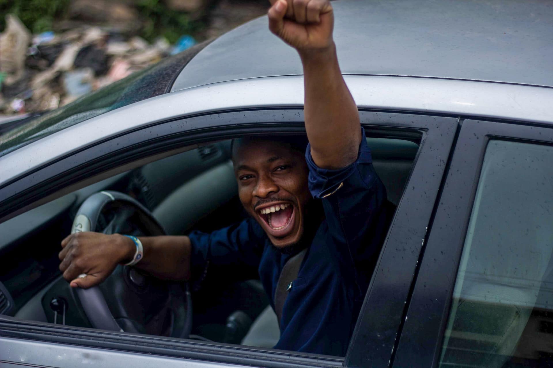 Homem negro levantando o braço de dentro do seu carro, comemorando vitória