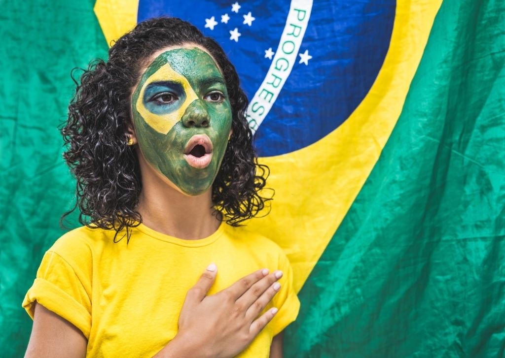 Torcedora brasileira colocando a mão no coração e cantando o hino nacional.