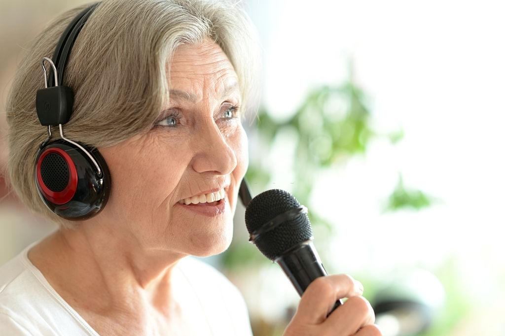 Mulher idosa cantando ao microfone usando fones de ouvido.