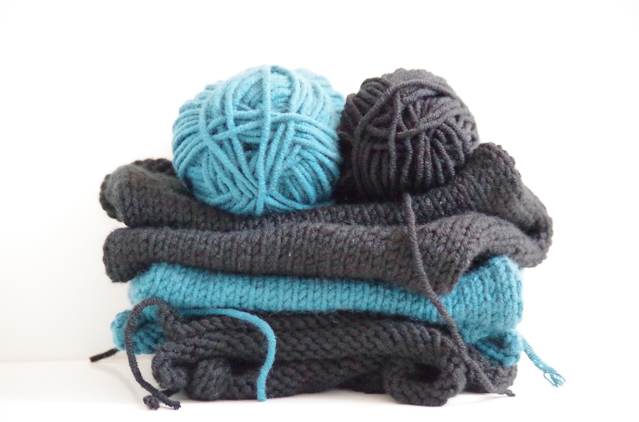 Peças de tricô azul e preto com novelos de lã