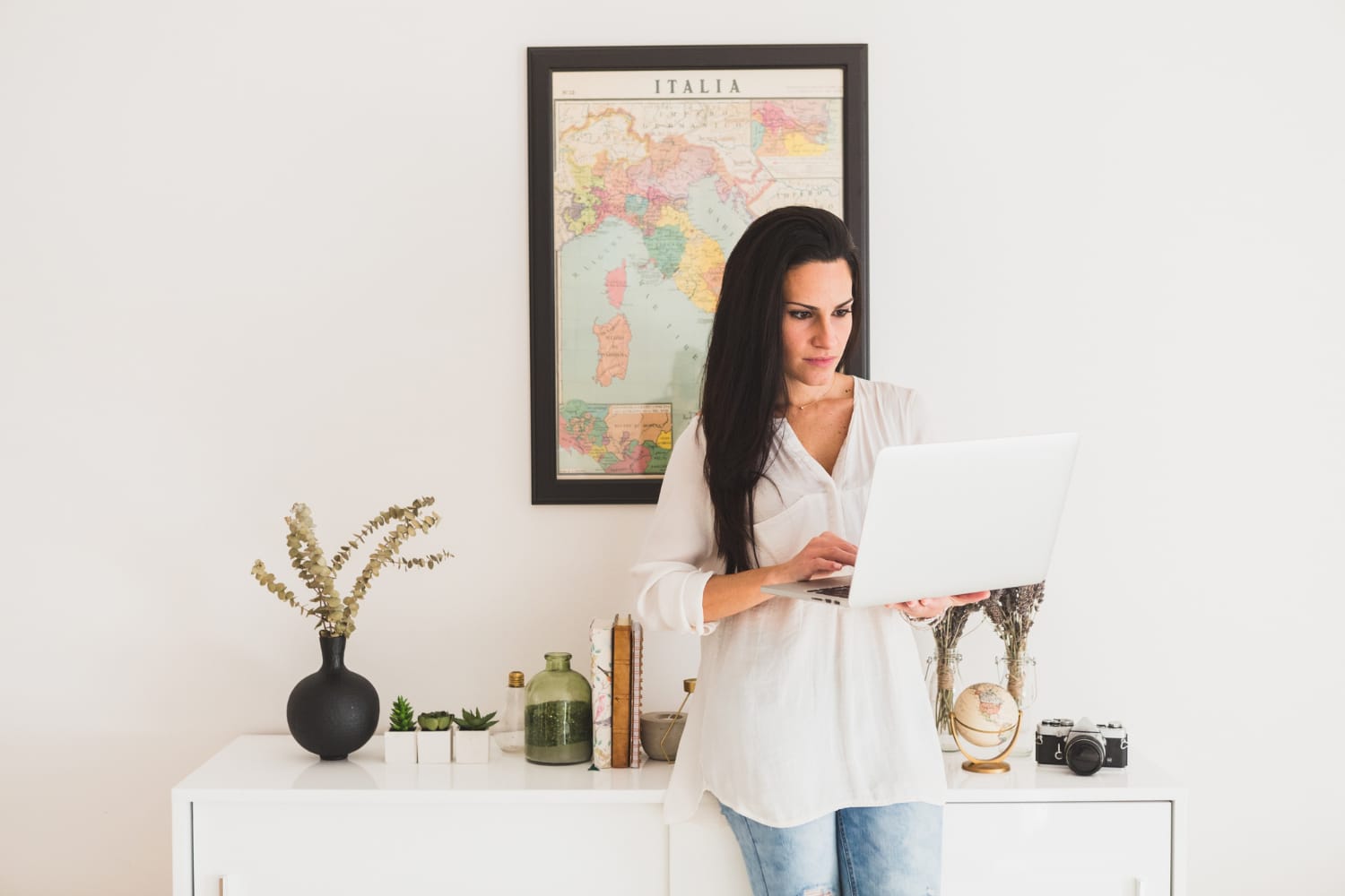 Mulher branca olhando no computador portátil e com mapa da italia na parede