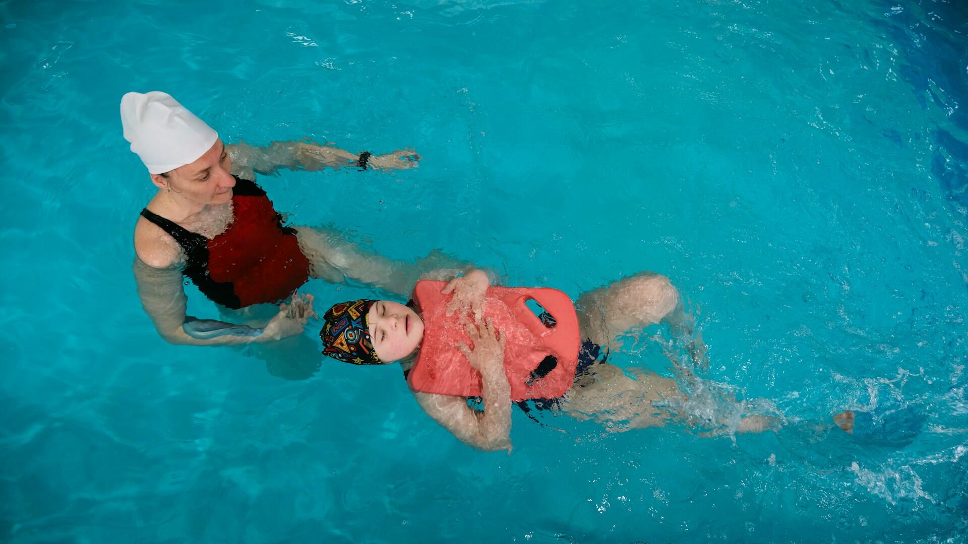 Adulto e criança em uma piscina com uma boia aprendendo a nadar