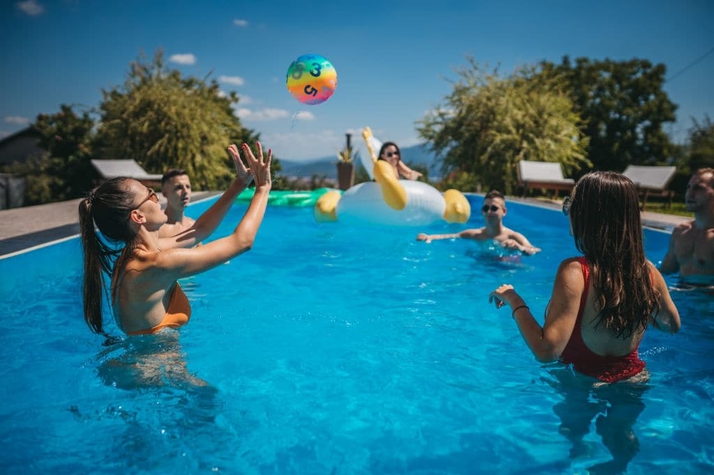 Grupo de jovens amigos brincando com bola de praia na piscina.