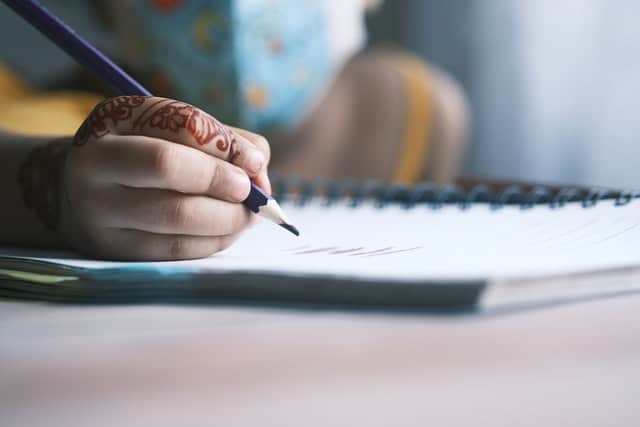 Mão segurando lápis e escrevendo no caderno