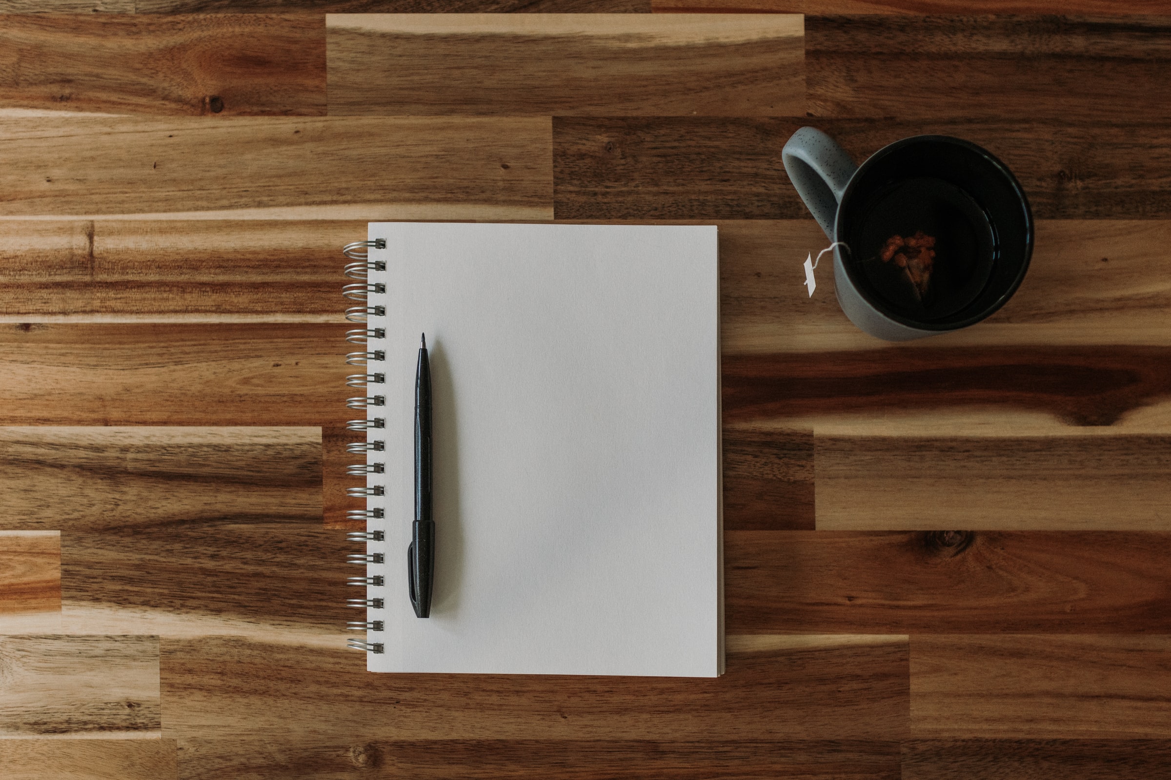 Caderno, caneta e xícara de chá em cima da mesa de madeira. 