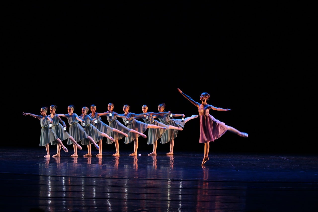 Uma bailarina com crianças dançando no palco.