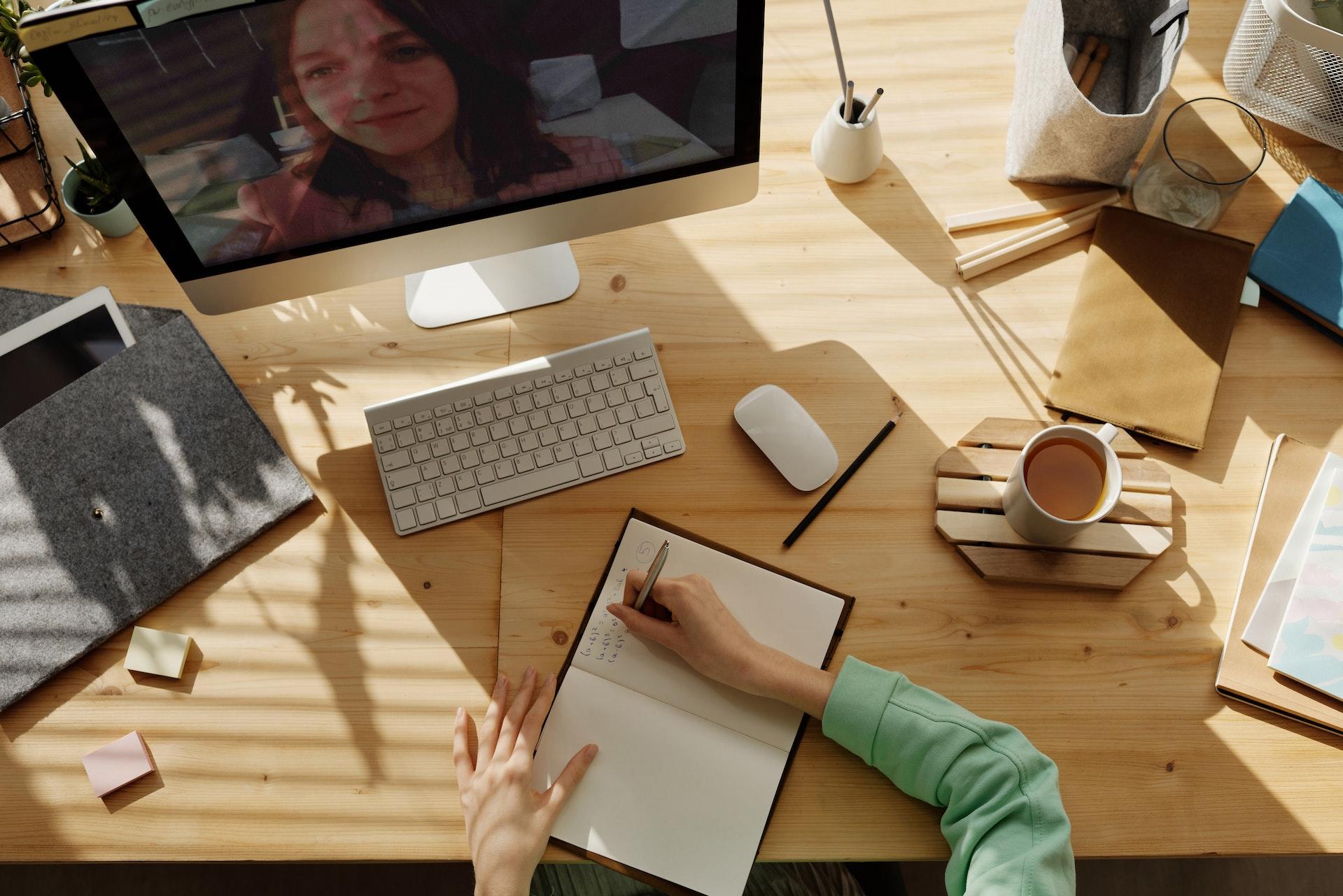 mesa com coisas espalhadas e uma pessoa escrevendo em um papel algo do computador