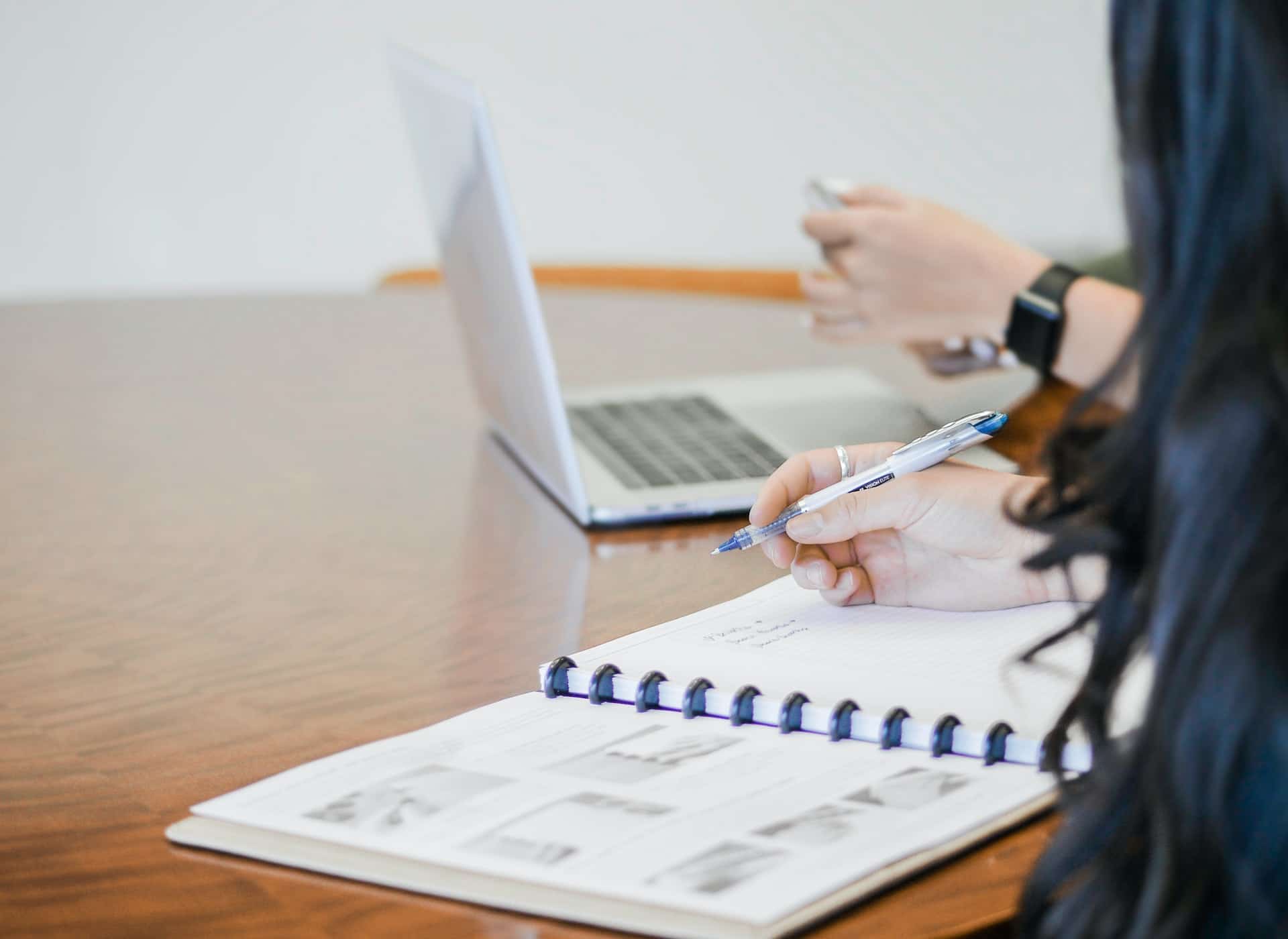 duas pessoas escrevendo, uma em um caderno e a outra em um computador