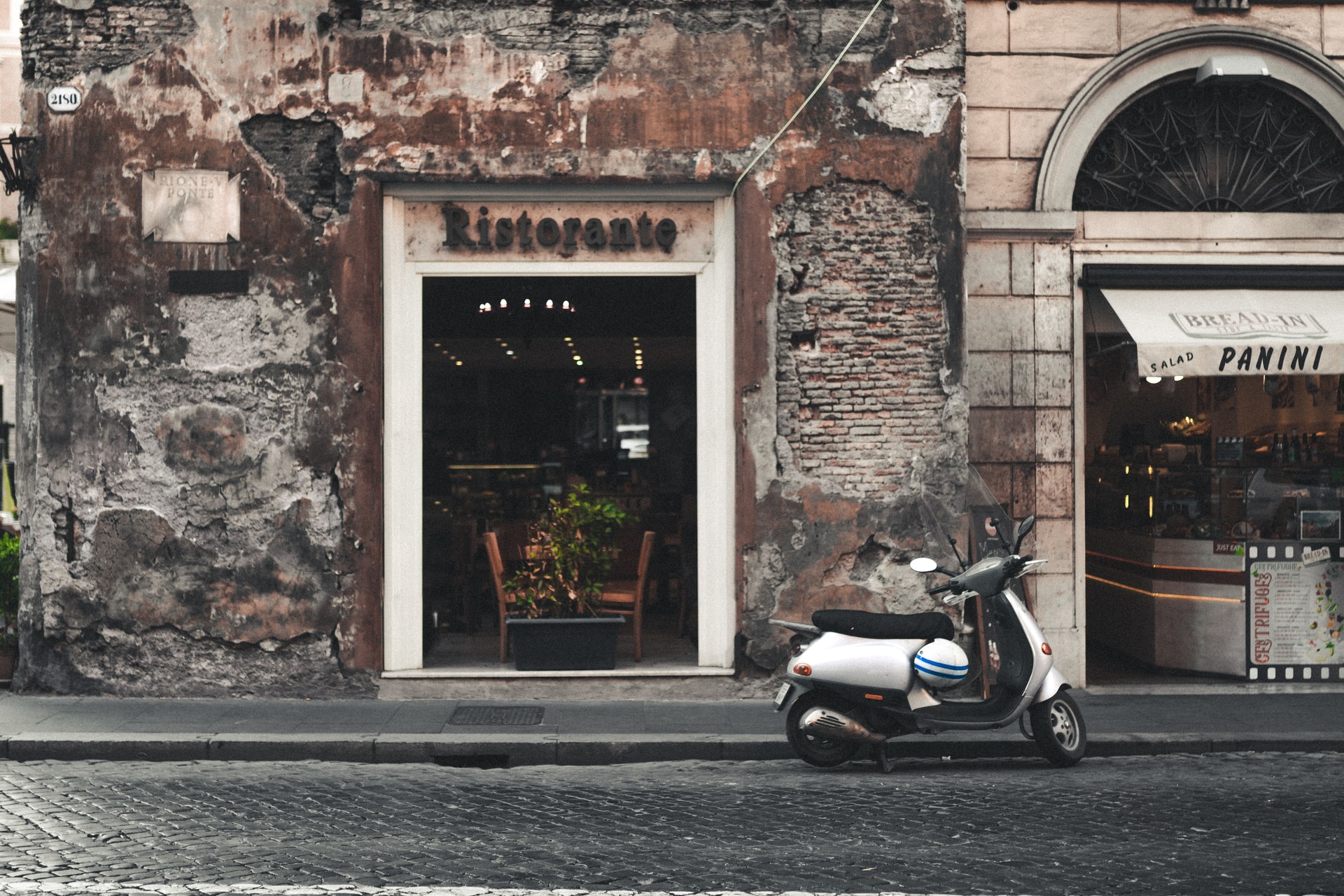 placa de restaurante em italiano com vespa estacionada na frente
