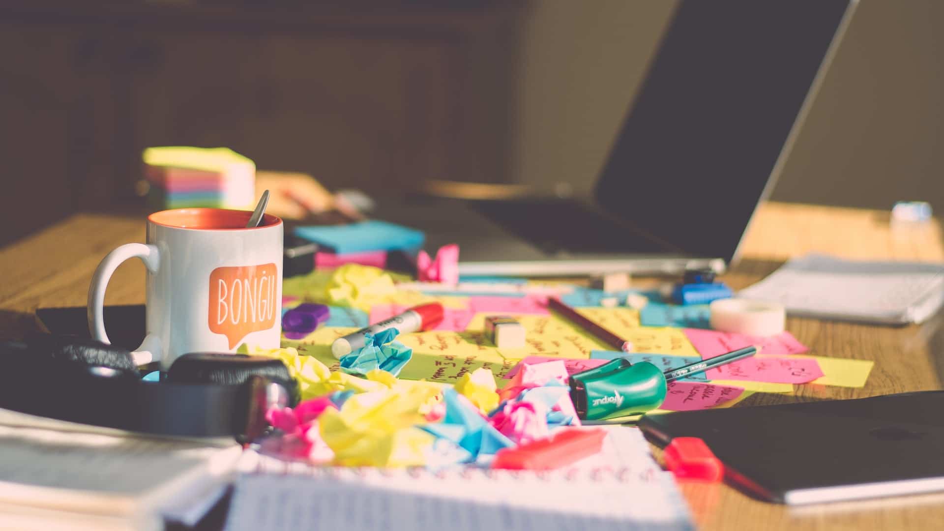 varios post-it coloridos amassados sob a mesa com uma taça de café e pc ao lado