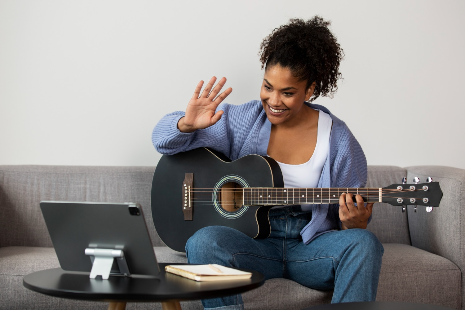 Profesora dando oi para aluno na aula on-line de violão.