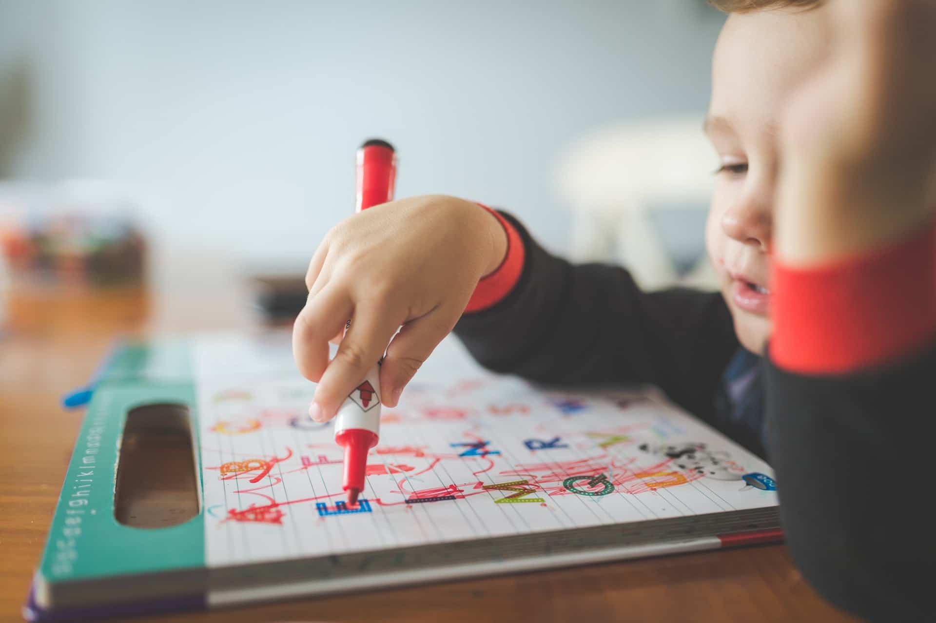 Menino desenha com canetinha sobre caderno.