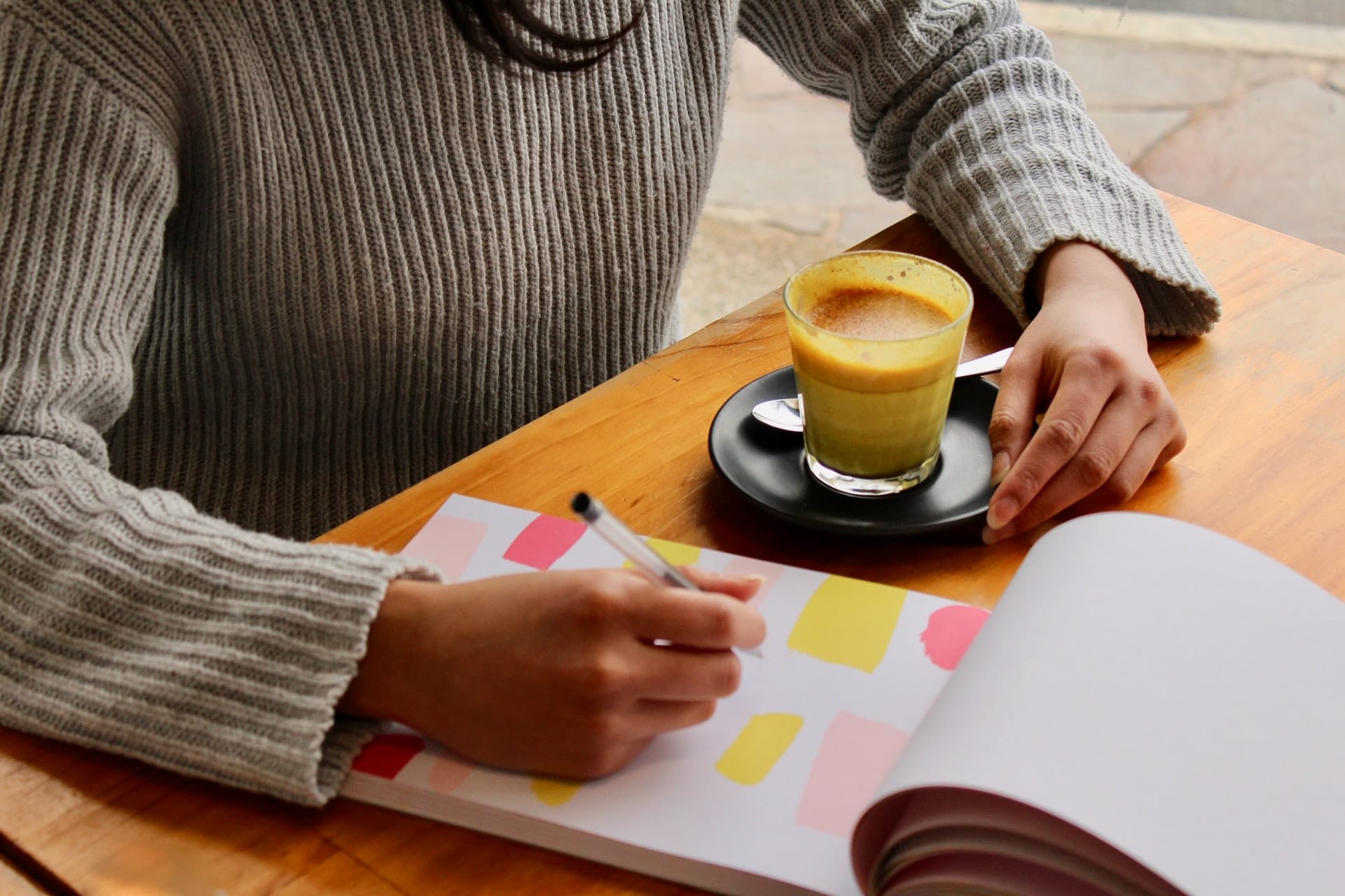Mãos escrevendo em caderno com um café ao lado 