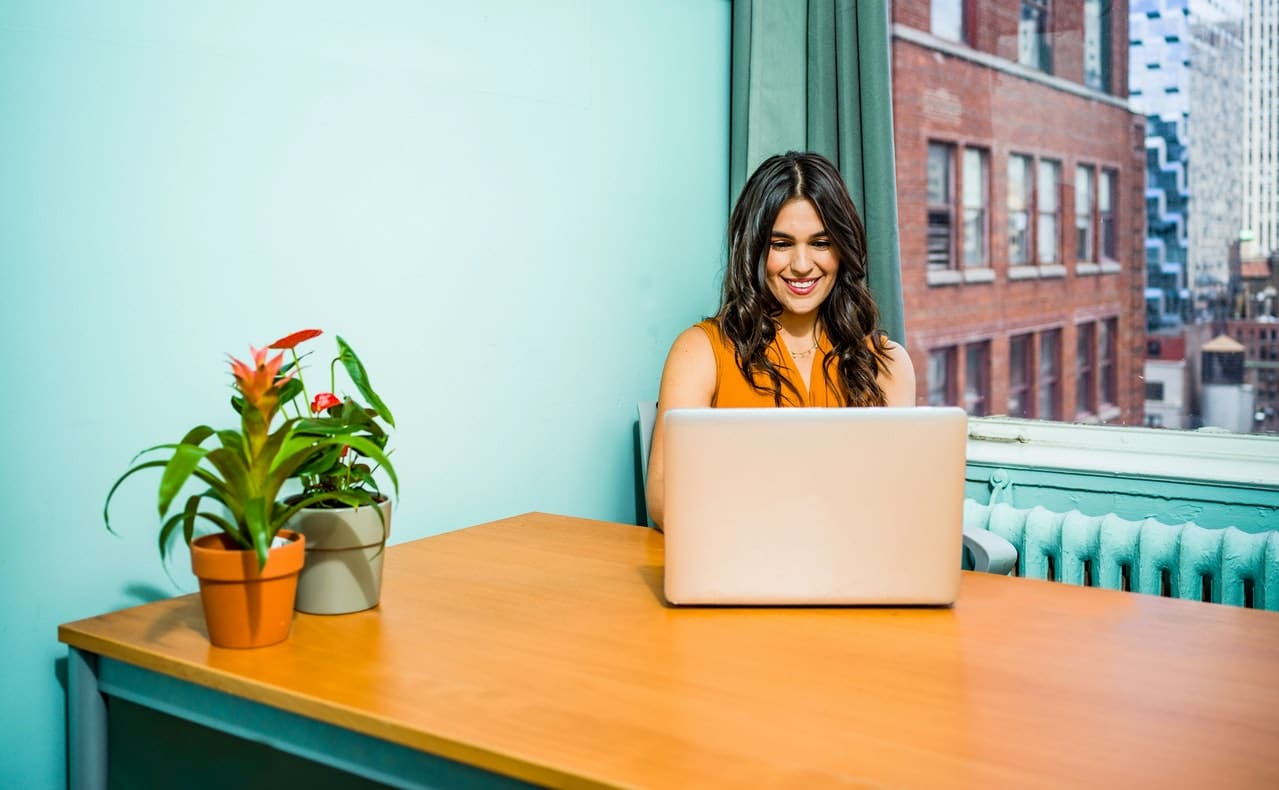 Mulher trabalha no computador com sorriso feliz no rosto