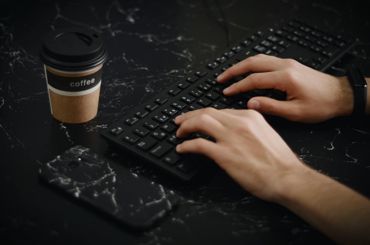 Teclado de computador preto sobre mesa preta e mão digitando