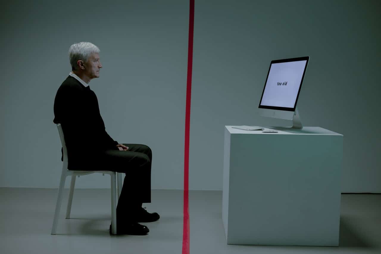 Idoso sentado na frente de uma tela de computador mac
