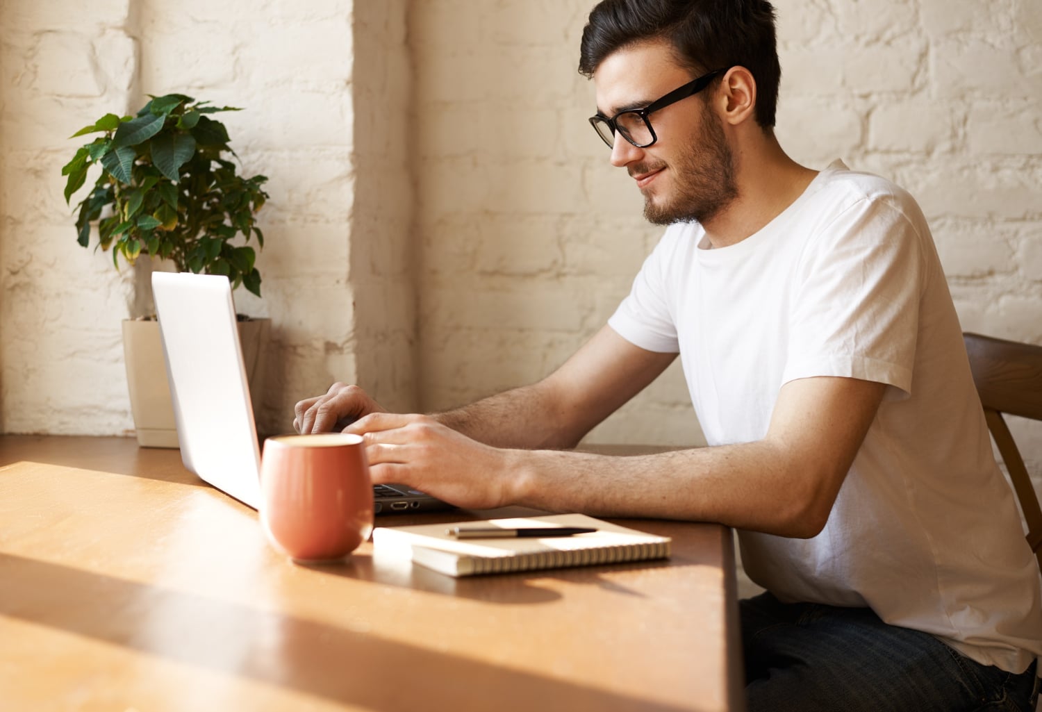 homem de óculos com um computador portátil digitando, tomando café e estudando