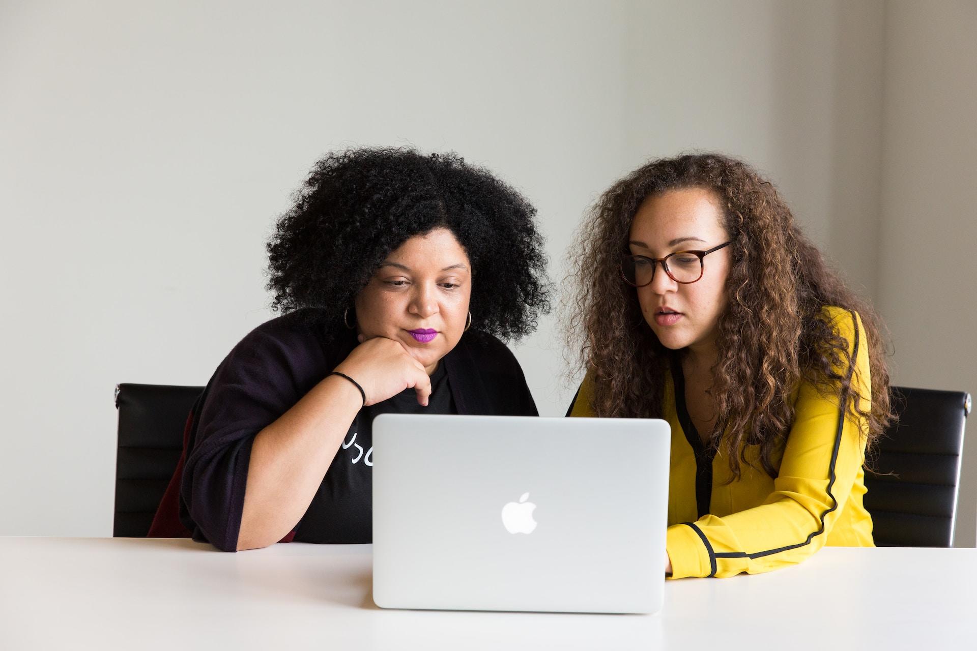 duas mulheres olhando para um pc da mac